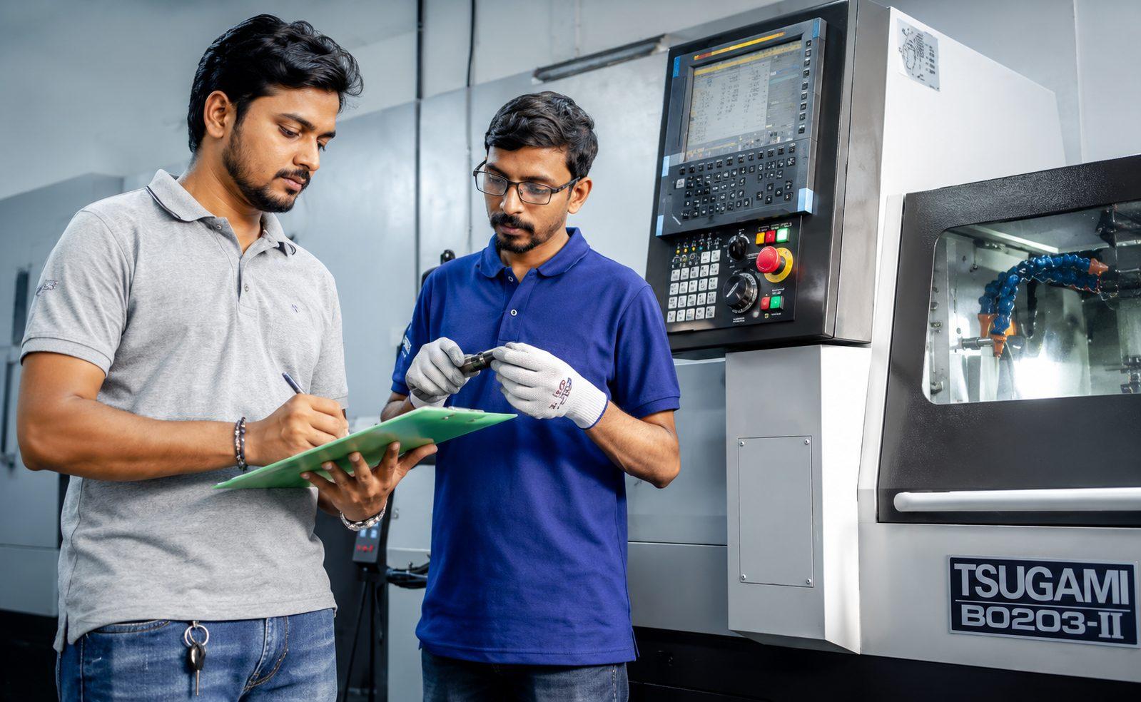Two RebarConnect engineers checking a machined coupler against the job sheet beside the CNC lathe